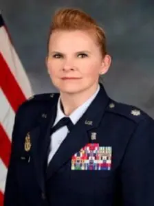 Military officer in uniform, American flag background.